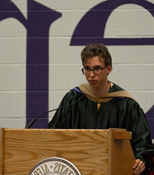 young mad with glasses, wearing robe, talking at podium