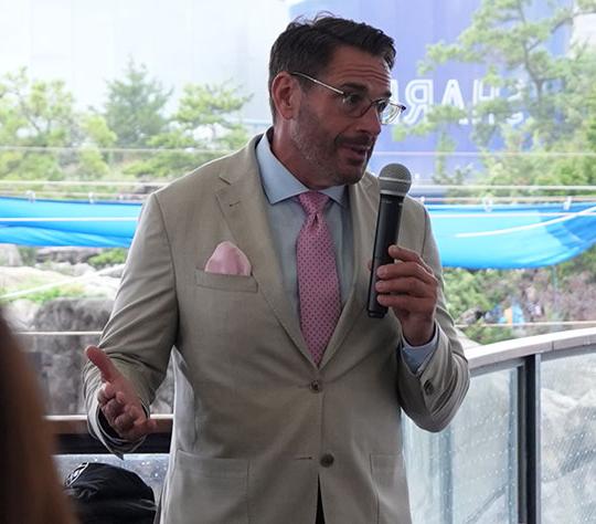 man with beard in suit, wearing glasses, talking with microphone